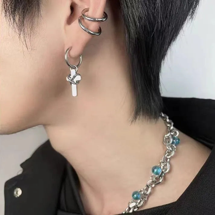 Person wearing stainless steel barbed cross hoop earrings with minimalist streetwear styling.