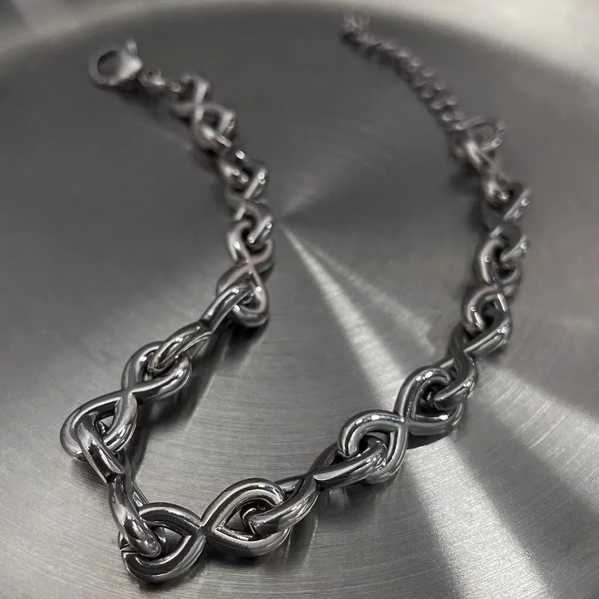 Infinity link stainless steel bracelet with polished silver finish and adjustable lobster clasp.